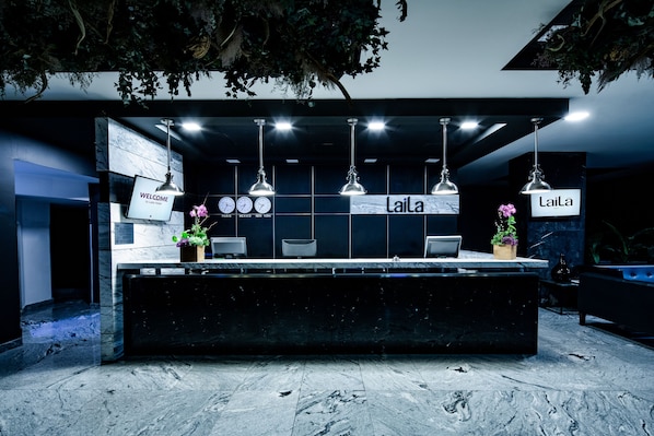 A reception desk with a 'Welcome' sign, a 'Laila' sign, and a digital clock displaying time in multiple cities. - Laila Hotel Mexico City Reforma (Mexico City)