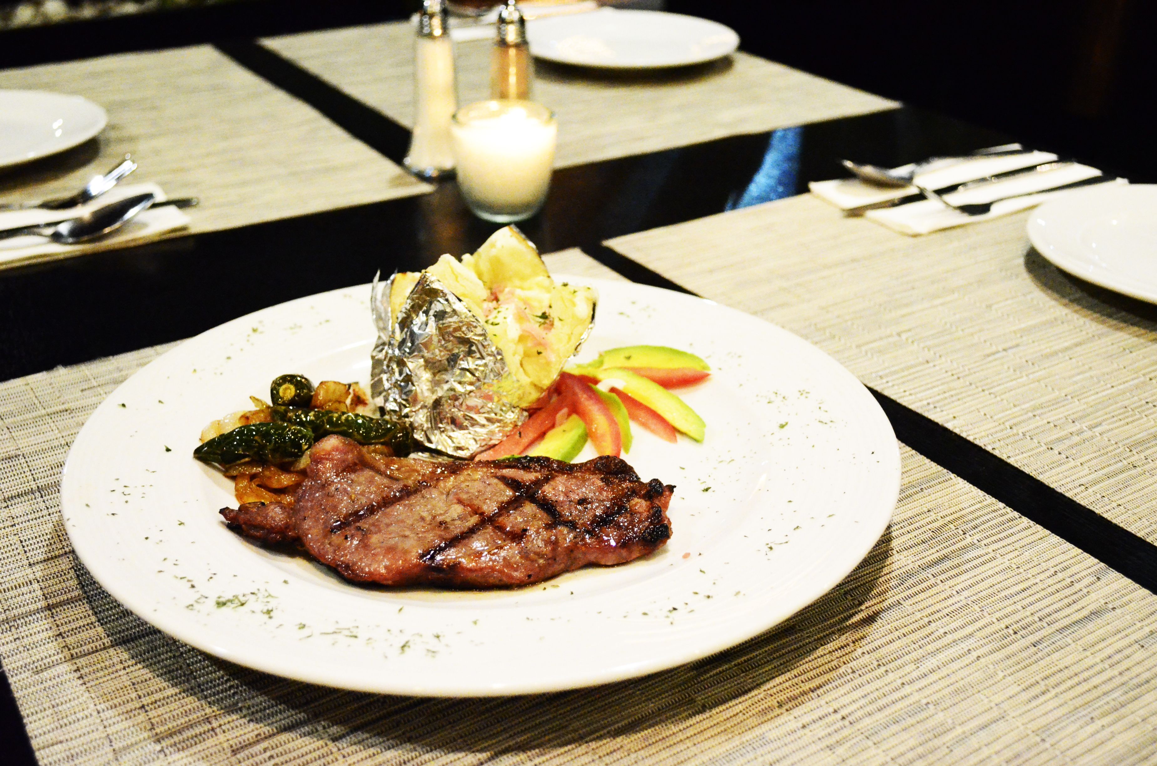 Une assiette contenant un steak, des légumes et un plat emballé dans du papier d’aluminium, le tout posé sur une table.
