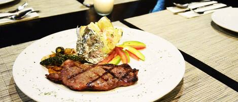 Un plato de comida con un filete, verduras y un alimento envuelto en papel de aluminio sobre una mesa.