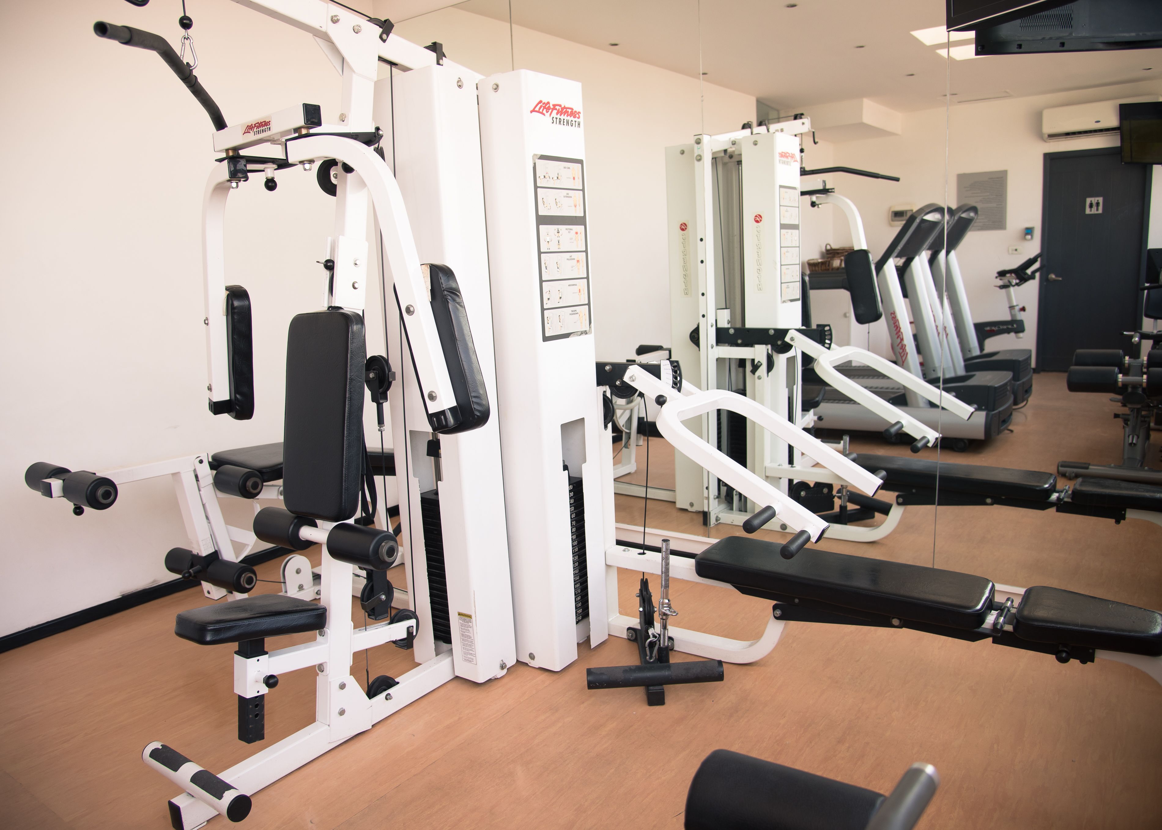 A gym with various exercise machines, a mirrored wall, and a door in the background.