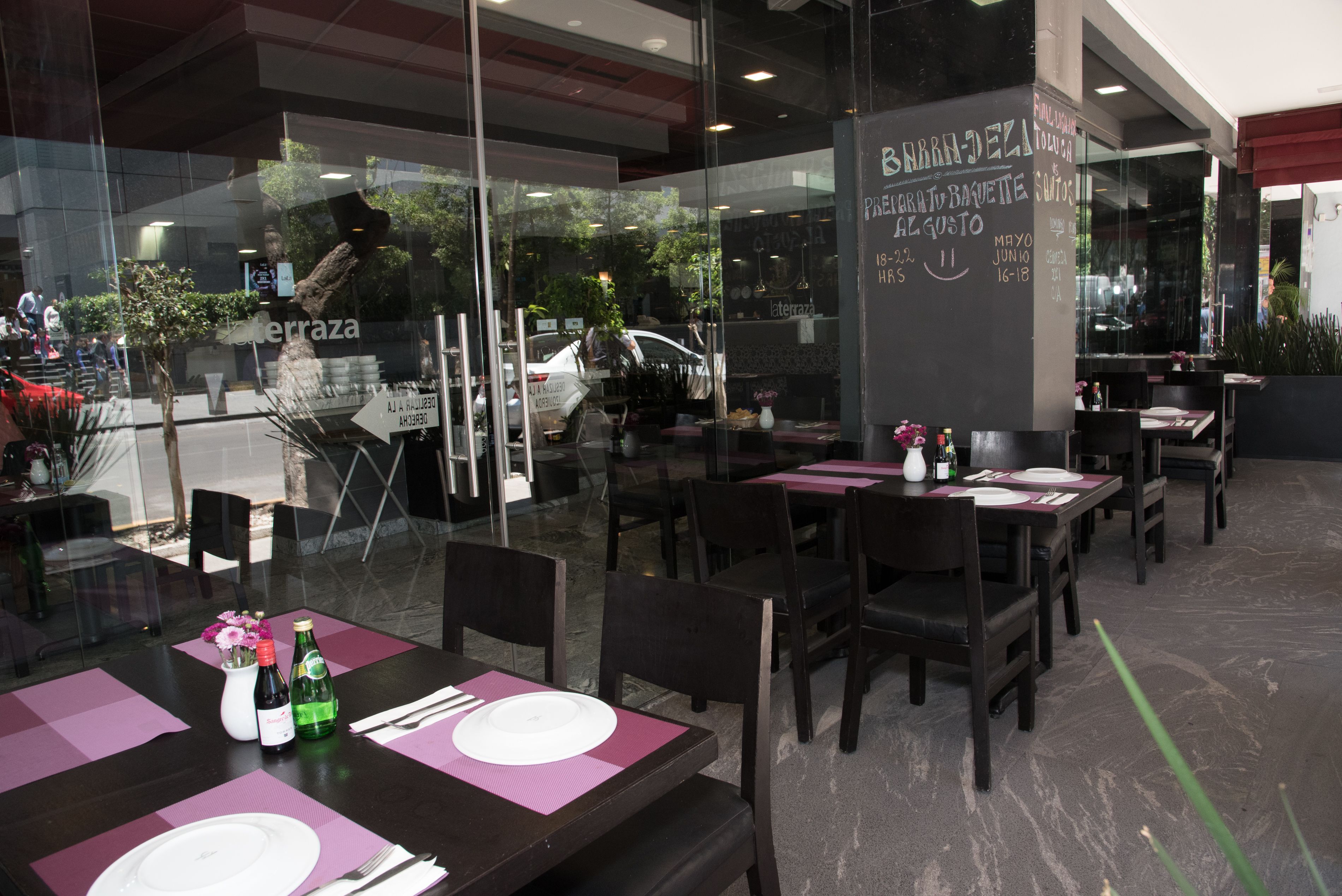 An outdoor dining area with tables set for two, featuring dark wooden chairs and purple placemats.