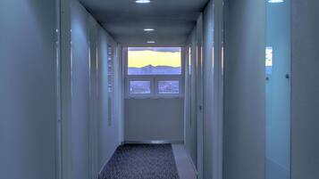 Un pasillo con pisos alfombrados, iluminación empotrada y una ventana al final.