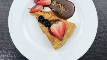 Sobremesa em prato branco com calda de chocolate, morangos e framboesas sobre superfície escura.