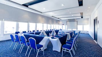 A conference room with blue chairs and tables, large windows, and a projector screen.