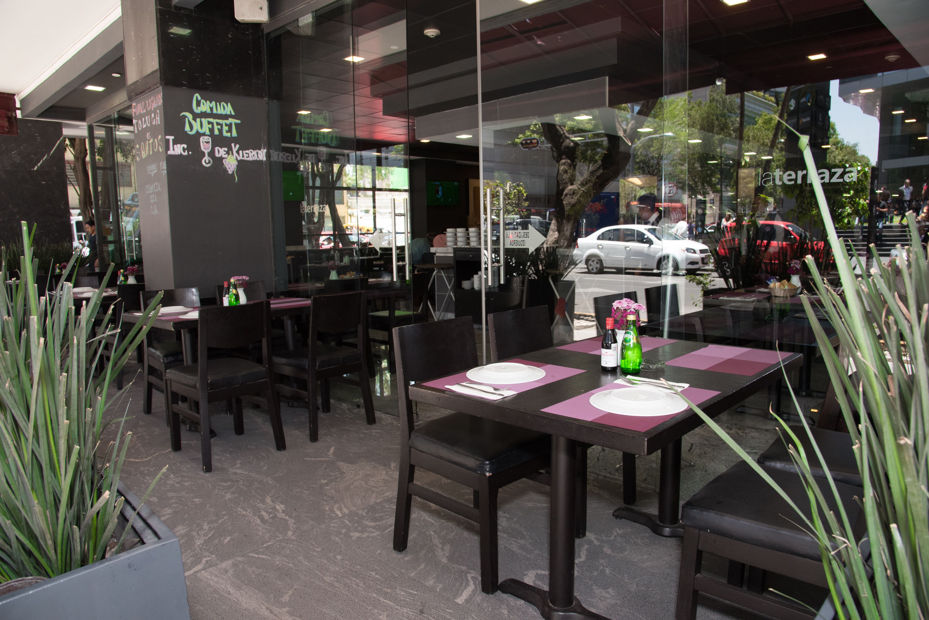 An outdoor dining area with tables set for two, chairs, and potted plants.