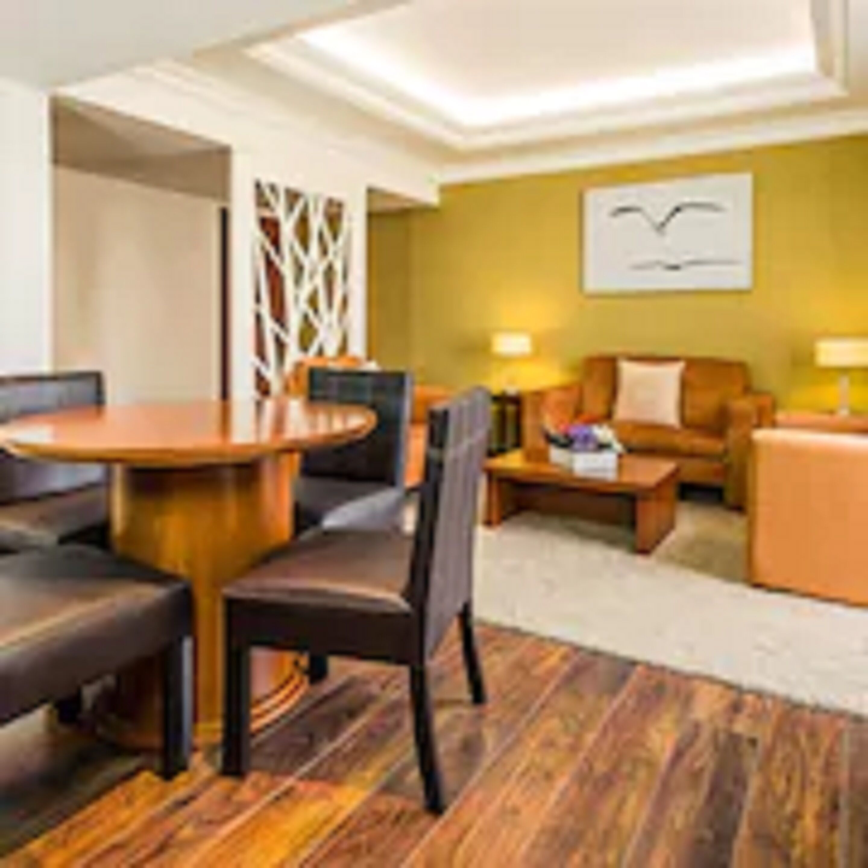 A modern hotel room with a wooden dining table, a sofa, and a coffee table.