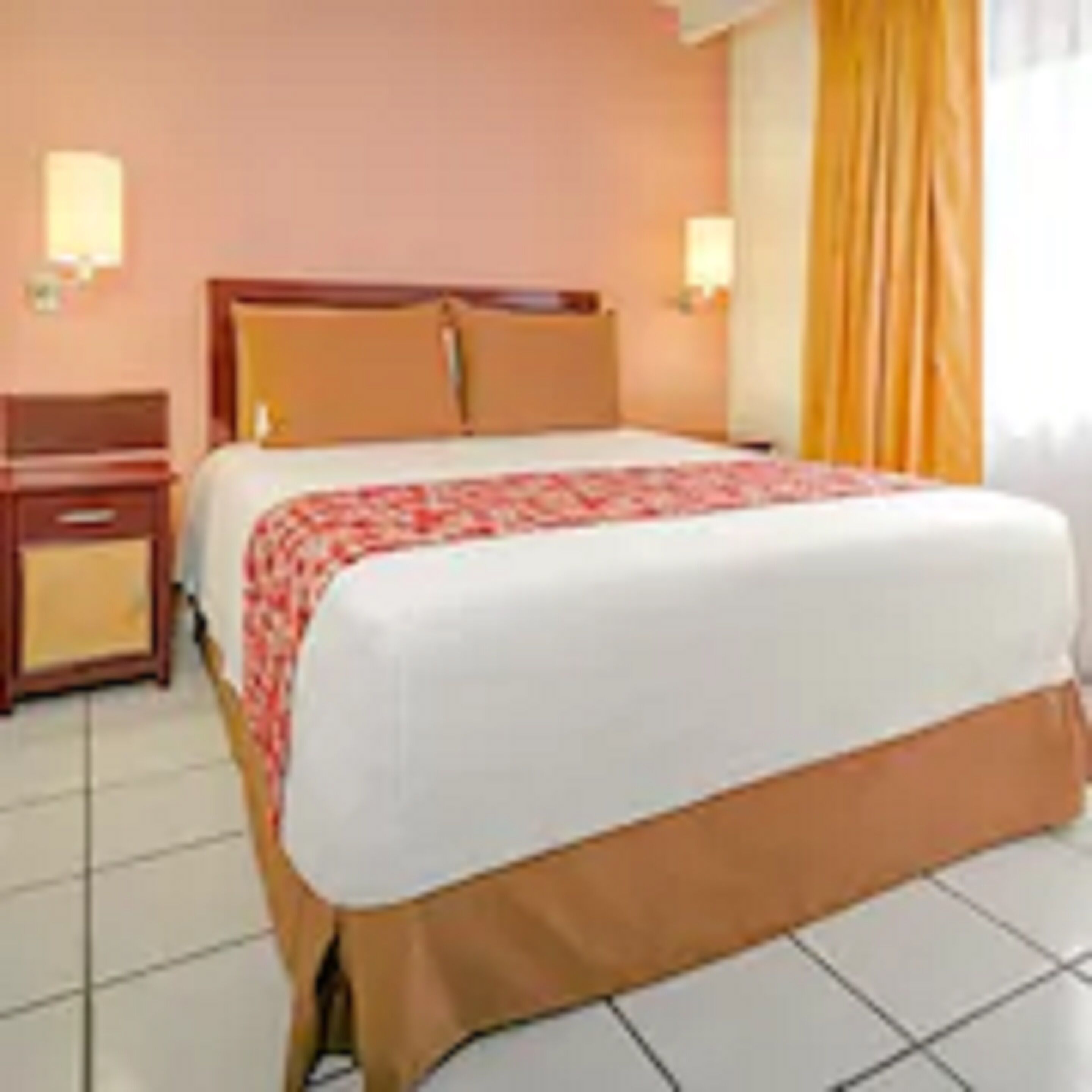 A hotel room with a bed, a nightstand, and a window with curtains.