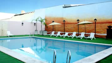 Una piscina al aire libre, sombrillas, sillones reclinables de piscina