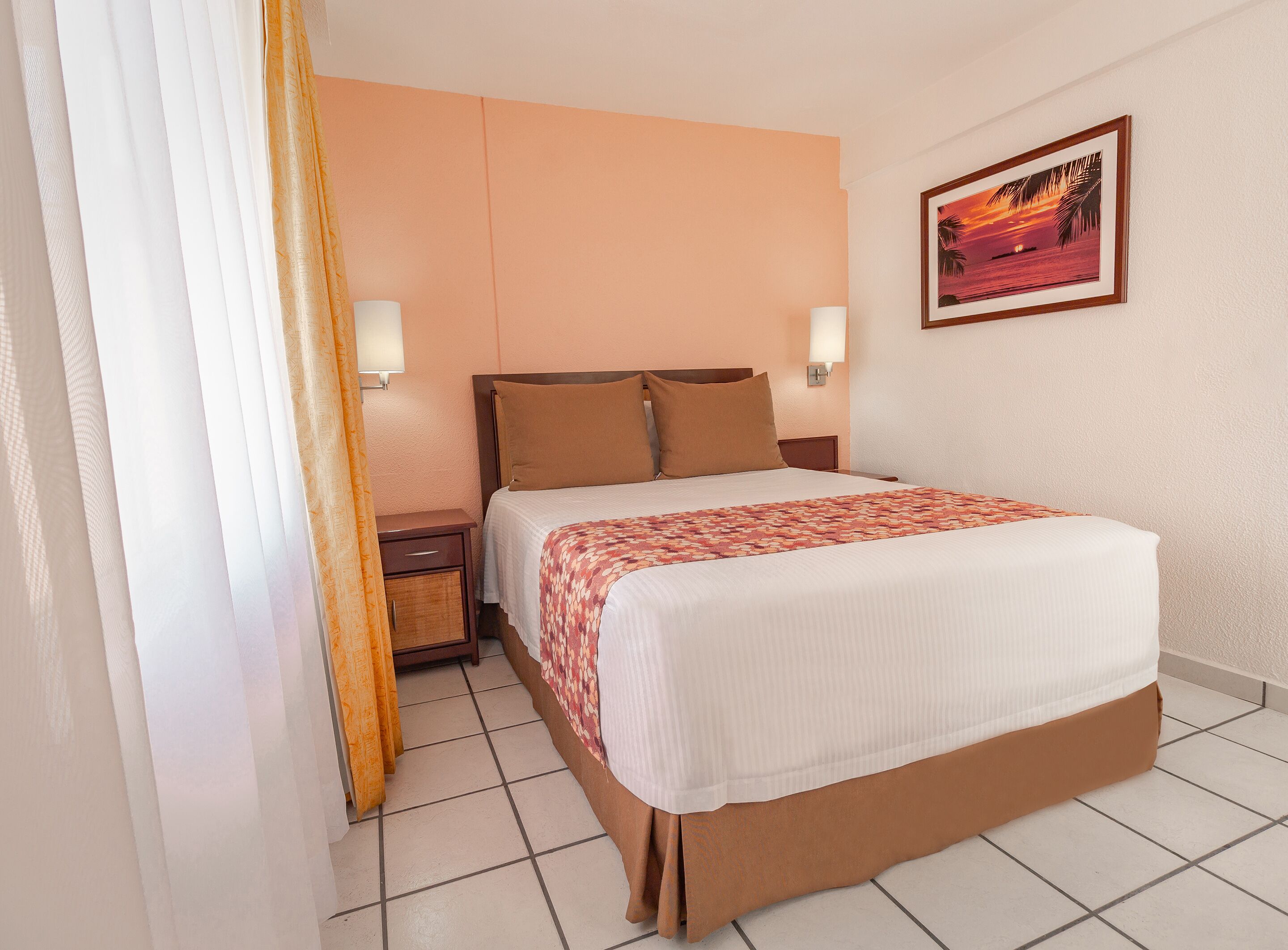 Una camera d'hotel con un letto, comodini, un quadro e una finestra con tende.