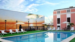 A swimming pool with lounge chairs and umbrellas, a mural of a sunset, and a building with a pink facade. - Veracruz Centro Histórico (Veracruz)