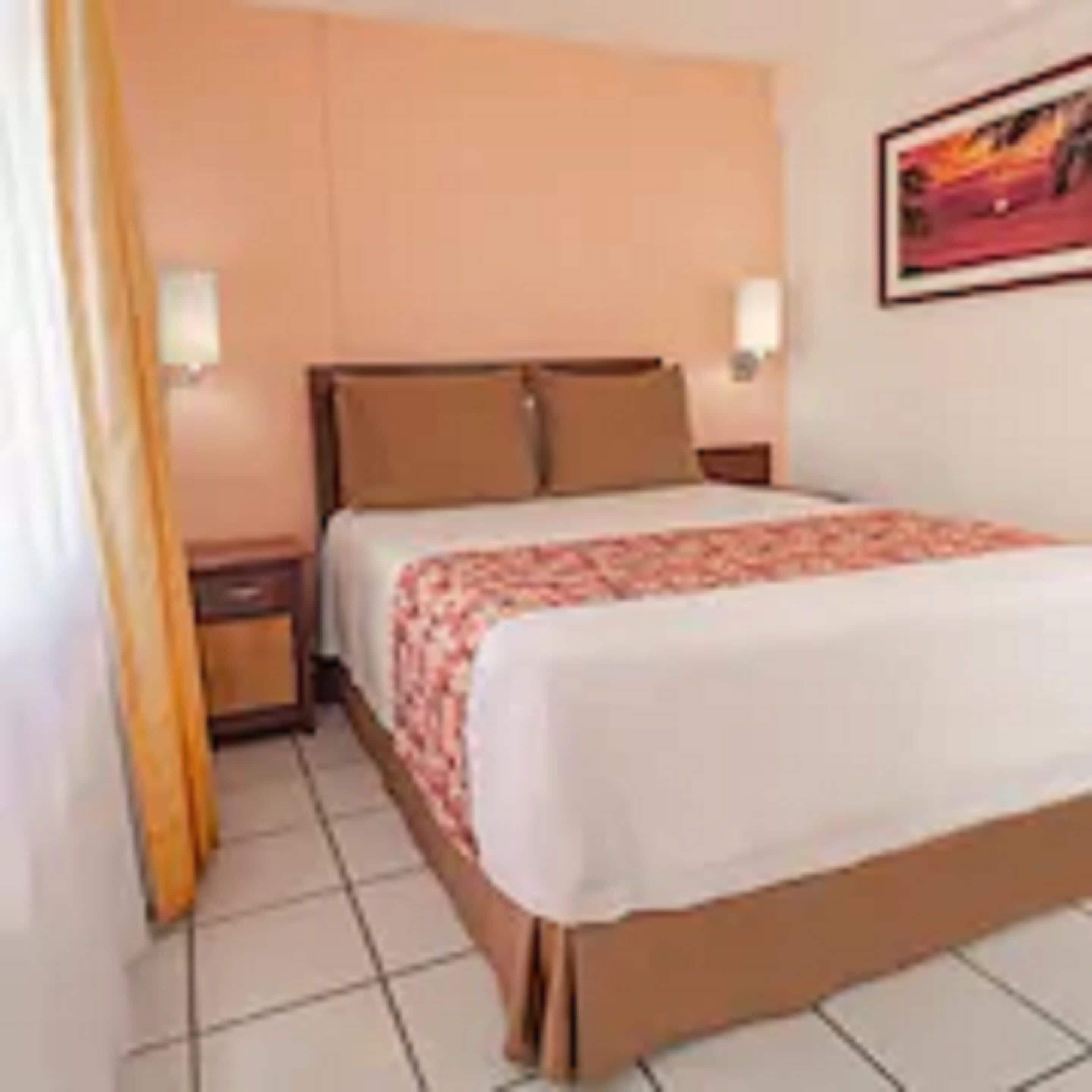 A hotel room with a bed, nightstands, a painting on the wall, and a curtain.