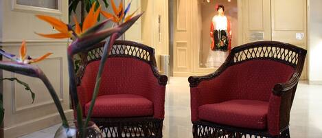 A reception area with two wicker chairs, a vase with flowers, and a framed botanical display.