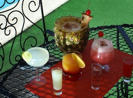 Una mesa con diversas bebidas, incluyendo un cóctel de piña, una bebida roja adornada con cereza y un vaso con rodaja de limón.