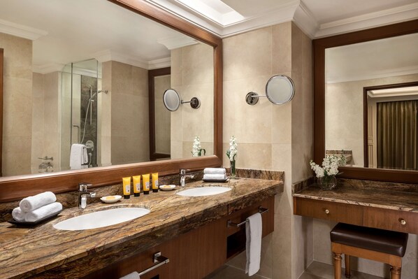 A bathroom with two sinks, a large mirror, and a vanity with a bench.