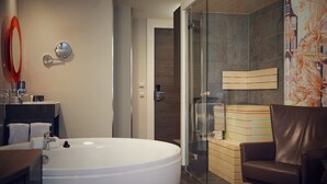 Un baño moderno con una bañera grande, cabina de ducha con mampara de vidrio y una butaca de cuero.