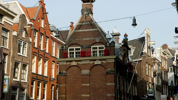 Un edificio histórico con fachadas de ladrillo rojo, ventanas arqueadas y un techo a dos aguas destacado.