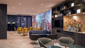 Una sala de estar moderna con una pared azul oscuro, un mural grande, un televisor de pantalla plana y una estantería con objetos decorativos.