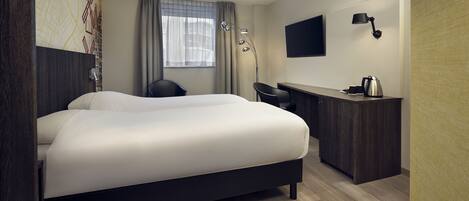 A modern hotel room with a large bed, a desk, a chair, a TV, and a coffee maker.