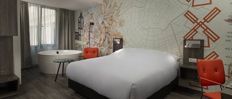 A modern hotel room with a large bed, a round bathtub, a desk, and a chair.