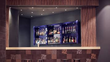 A bar area with shelves of liquor bottles, a counter, and bar stools.