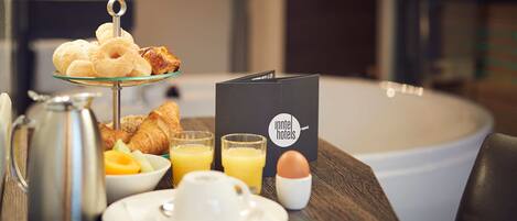A breakfast setup with croissants, fruit, juice, and a coffee pot on a table.