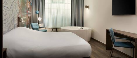 A hotel room with a large bed, a desk, a chair, a round bathtub, and a TV on the wall.
