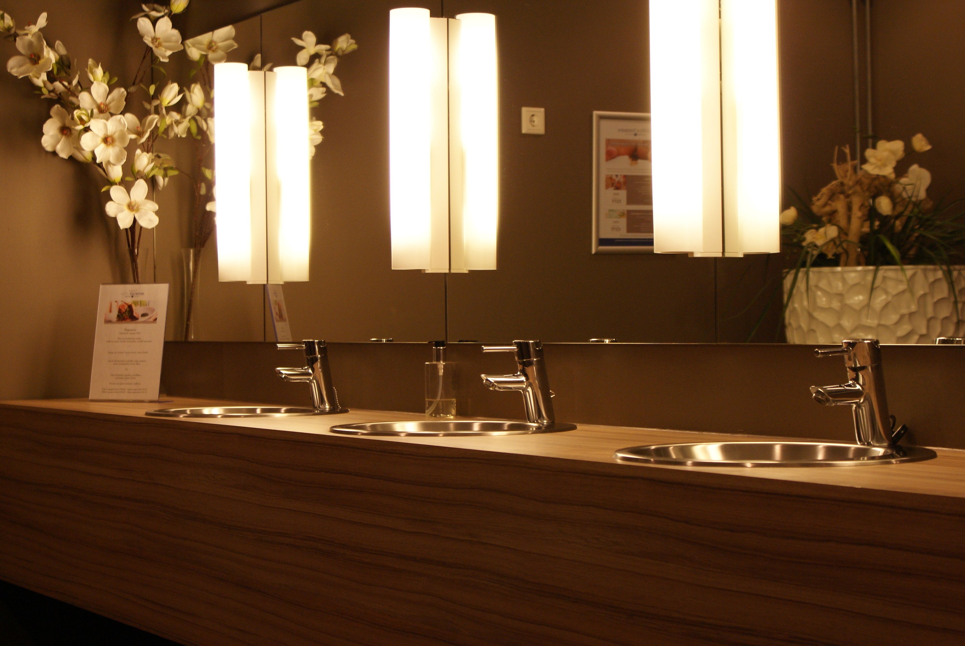 Un baño de hotel con tres lavamanos, un espejo y un jarrón de flores blancas.