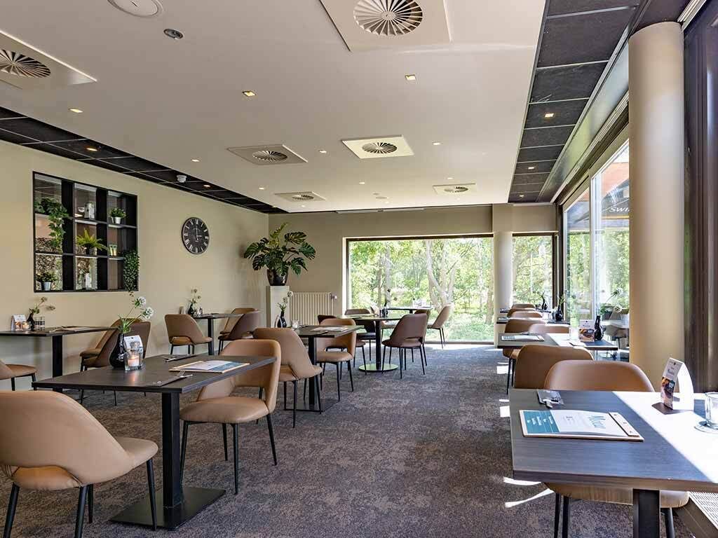 A modern hotel lobby with multiple seating areas, a reception desk, and large windows offering a view of the outdoors.