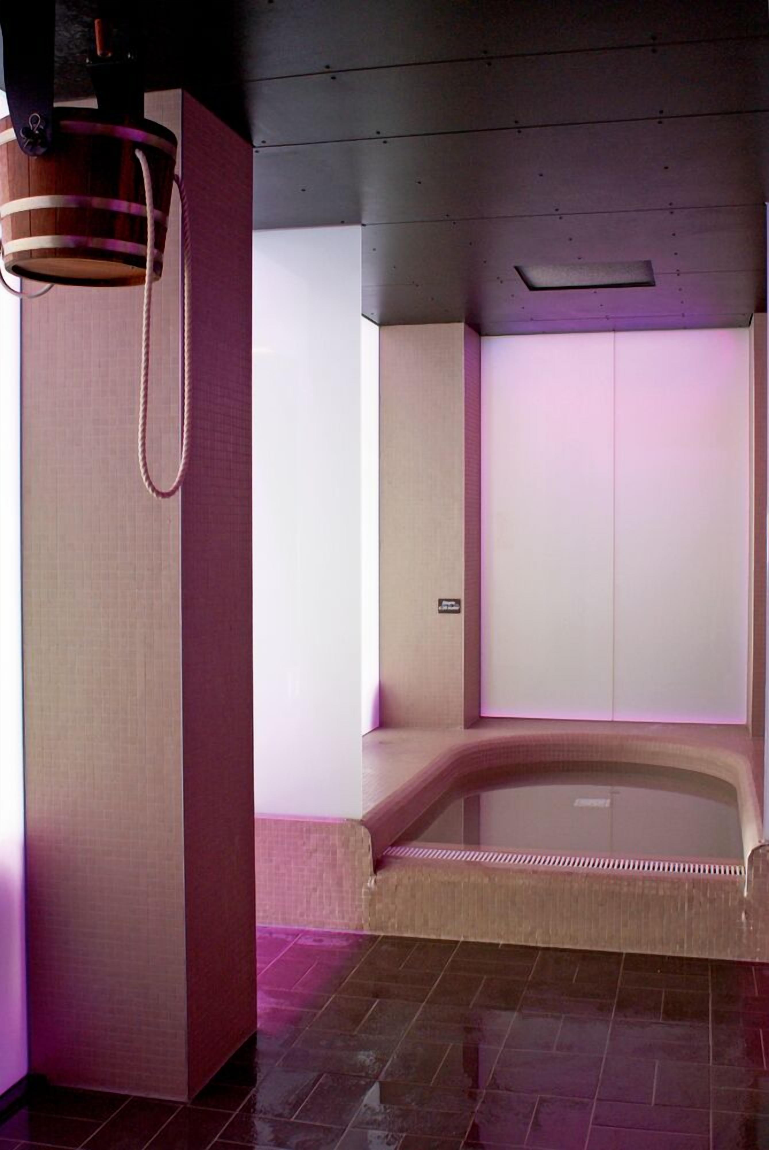 Un cuarto de spa con una camilla de masaje, un balde de madera y una silla de masaje fijada a la pared.