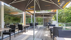 Un patio al aire libre con mesas y sillas, cubierto por sombrillas, y un muro de piedra al fondo.