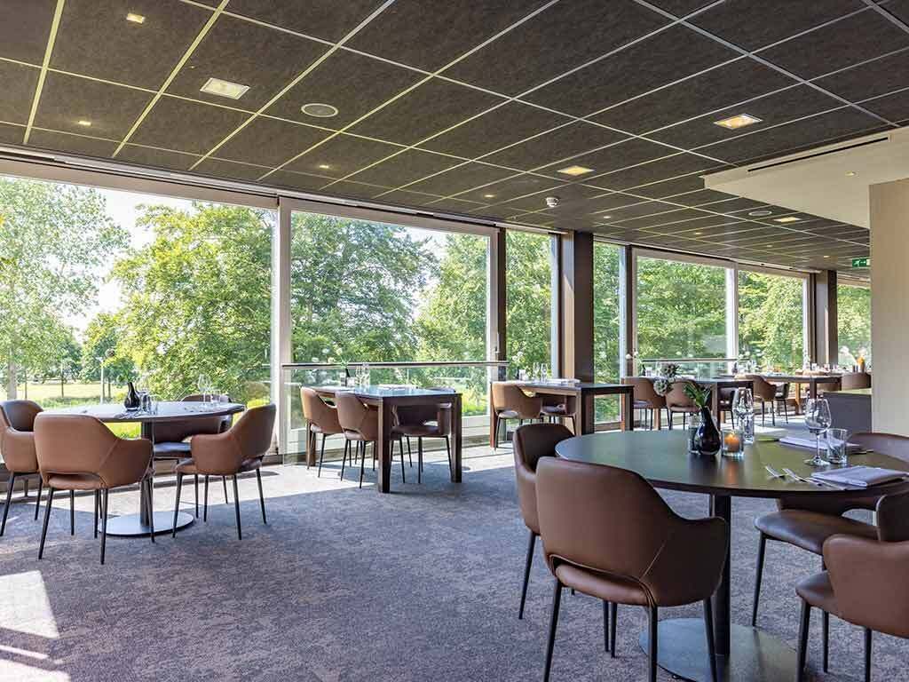 Een vergaderzaal met grote ramen, meerdere tafels en stoelen.
