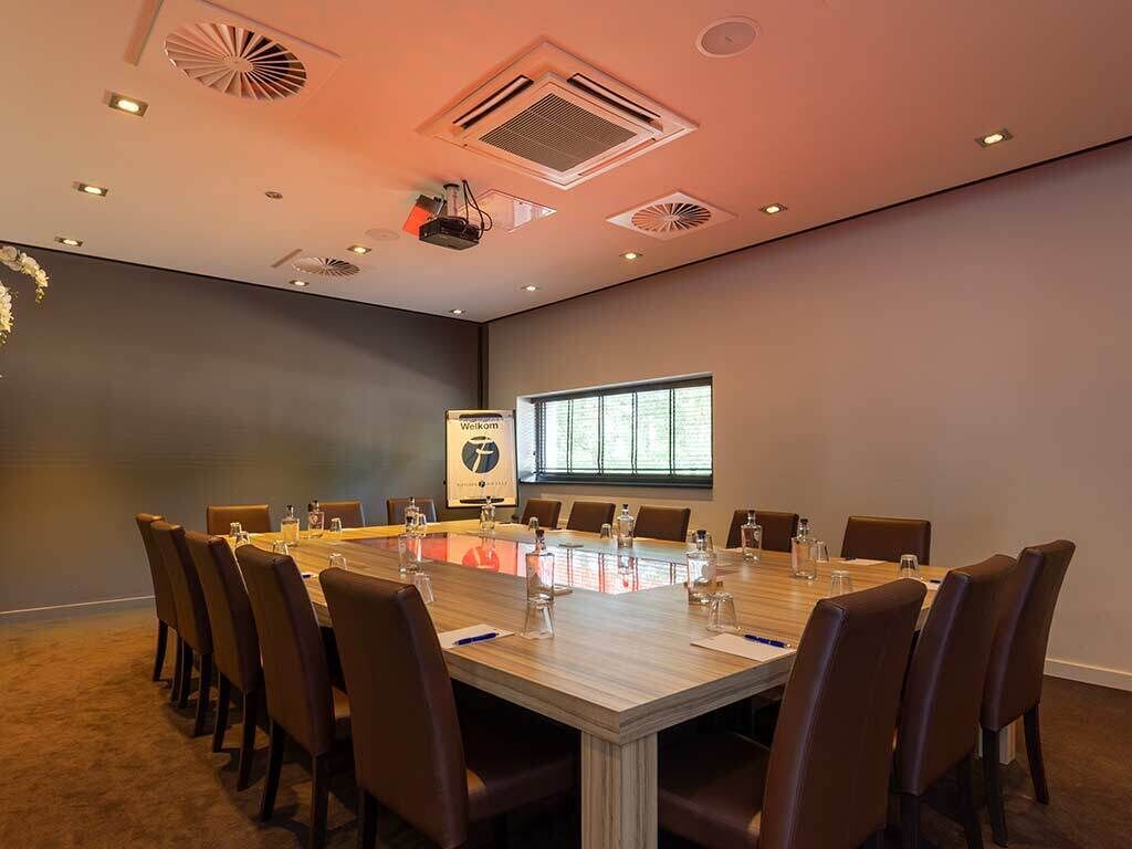 A conference room with a long table, chairs, and a projector screen.