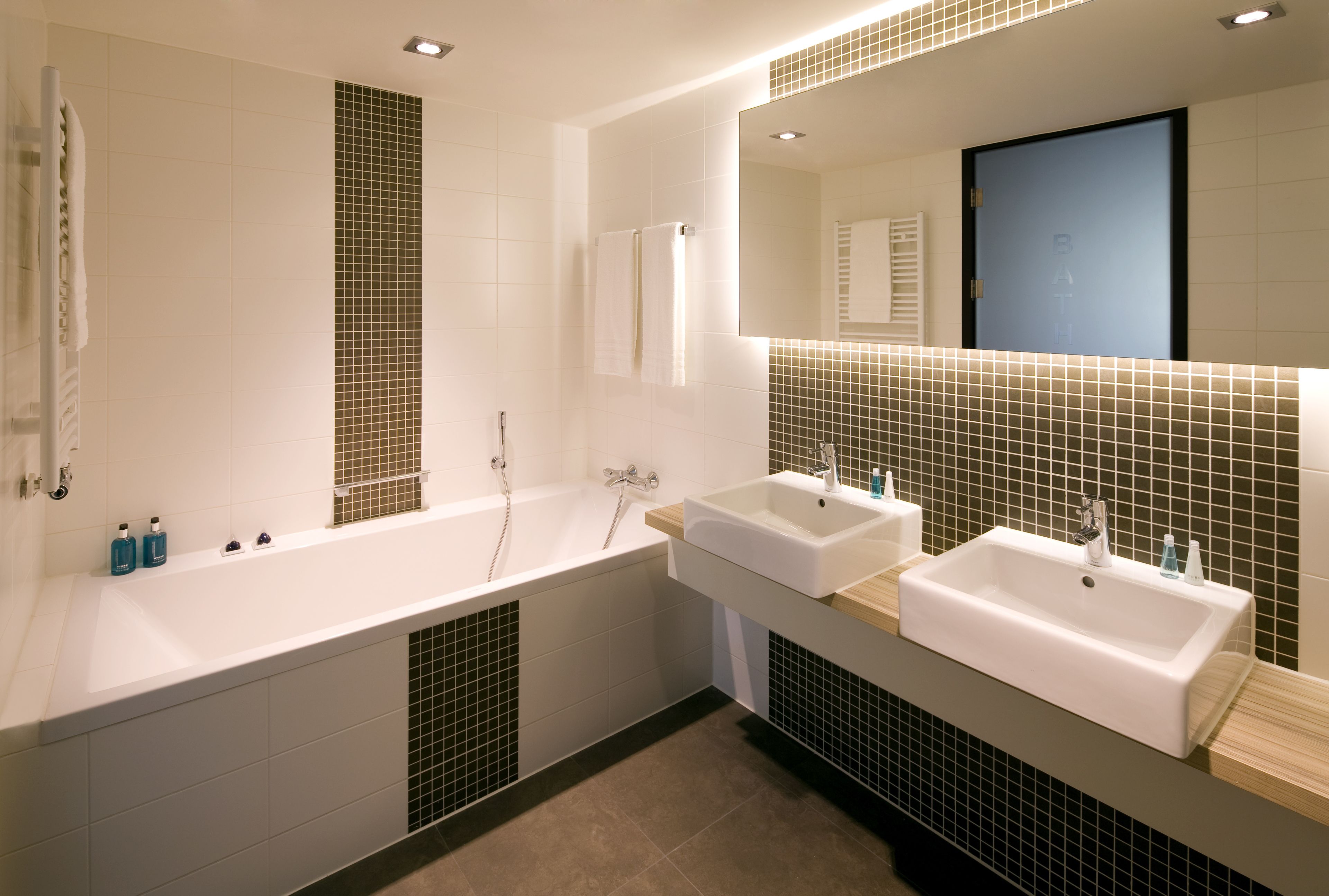 Un baño moderno con bañera, dos lavamanos y un espejo grande.