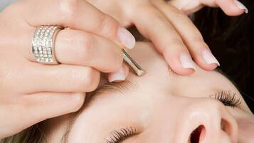 A close-up of a person's hands performing a beauty treatment, focusing on the forehead and hair.