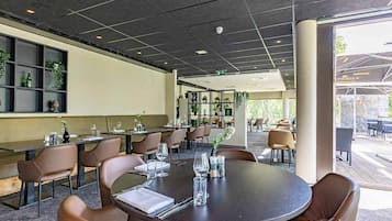 A modern indoor dining area with round tables and leather chairs, featuring a neutral color scheme and natural light from large windows.