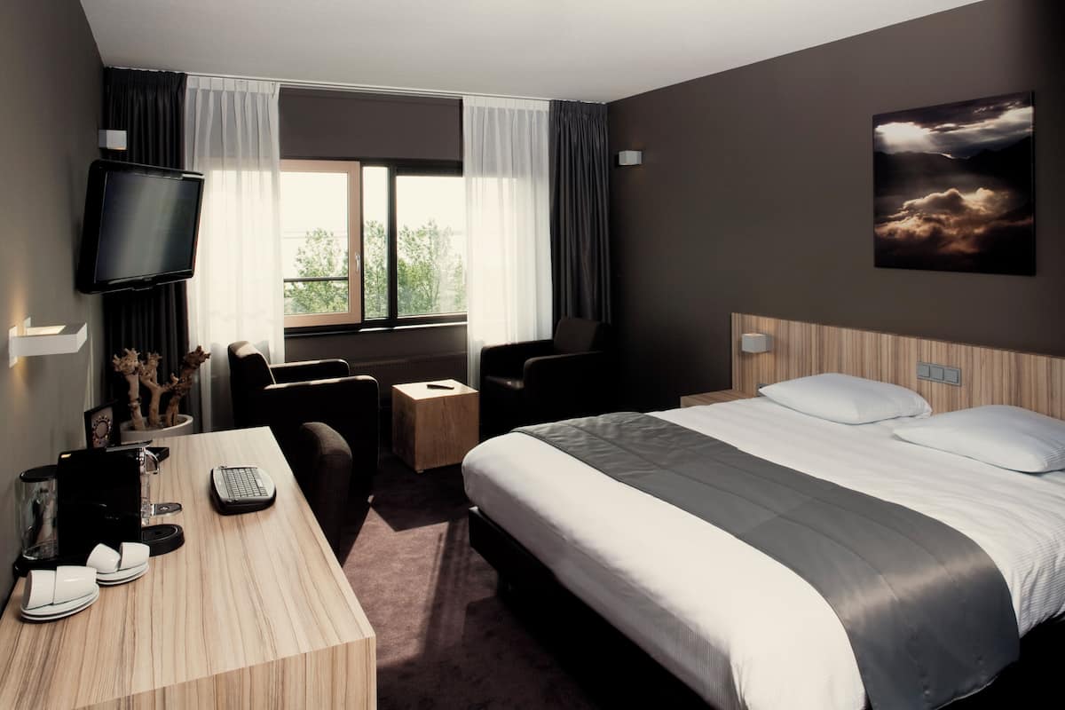 Ein Hotelzimmer mit Bett, Schreibtisch, Stuhl, Fernseher und einem Fenster mit Vorhängen.