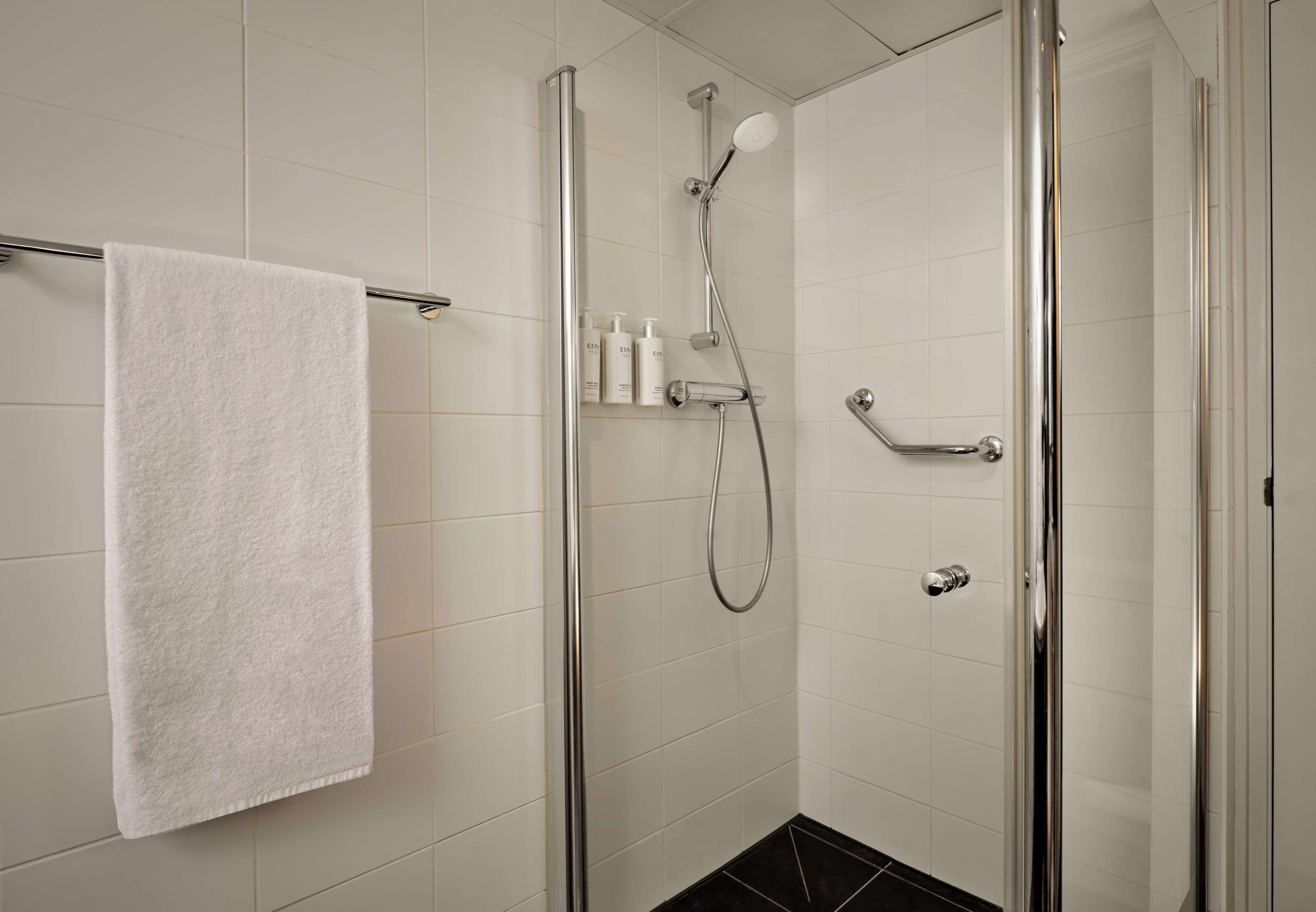 A modern shower with a handheld showerhead, a glass-enclosed shower stall, and a white towel hanging on a metal towel bar.