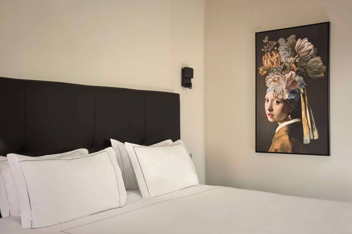 Une chambre à coucher avec un grand lit, une literie blanche, une tête de lit sombre et un tableau encadré accroché au mur.