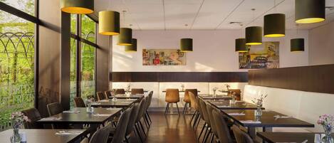 A restaurant with long tables, chairs, and hanging pendant lights.