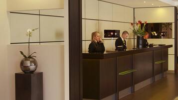 A reception desk with three staff members, a vase with flowers, and a modern interior design.