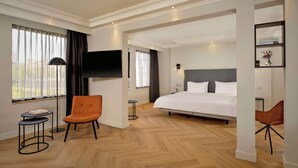 Ein Hotelzimmer mit einem großen Bett, zwei Sesseln, einem Fernseher und einem kleinen Tisch.