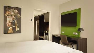 Habitación de hotel con cama, escritorio, silla, televisor y un cuadro en la pared.