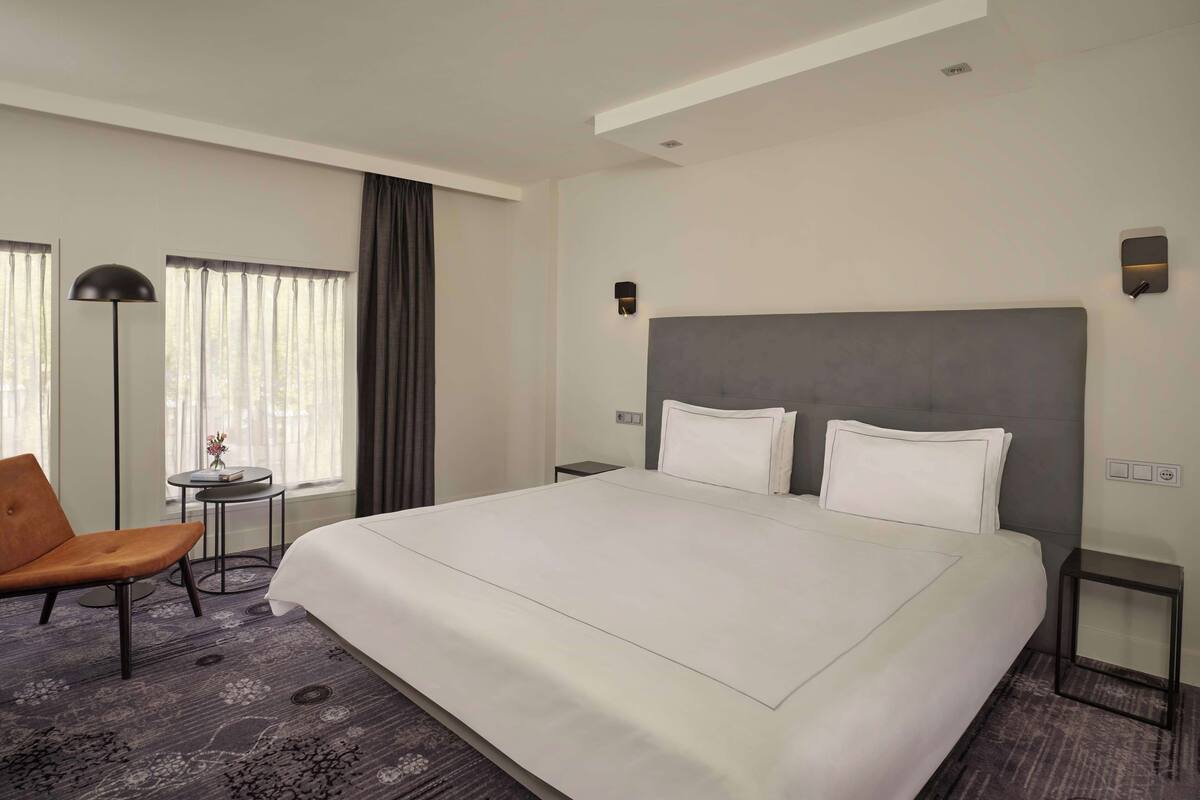 Une chambre d’hôtel moderne avec un grand lit, une chaise, une petite table et une lampe.