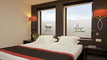A hotel room with a large bed, two bedside tables, a nightstand, and a window with a view of buildings.