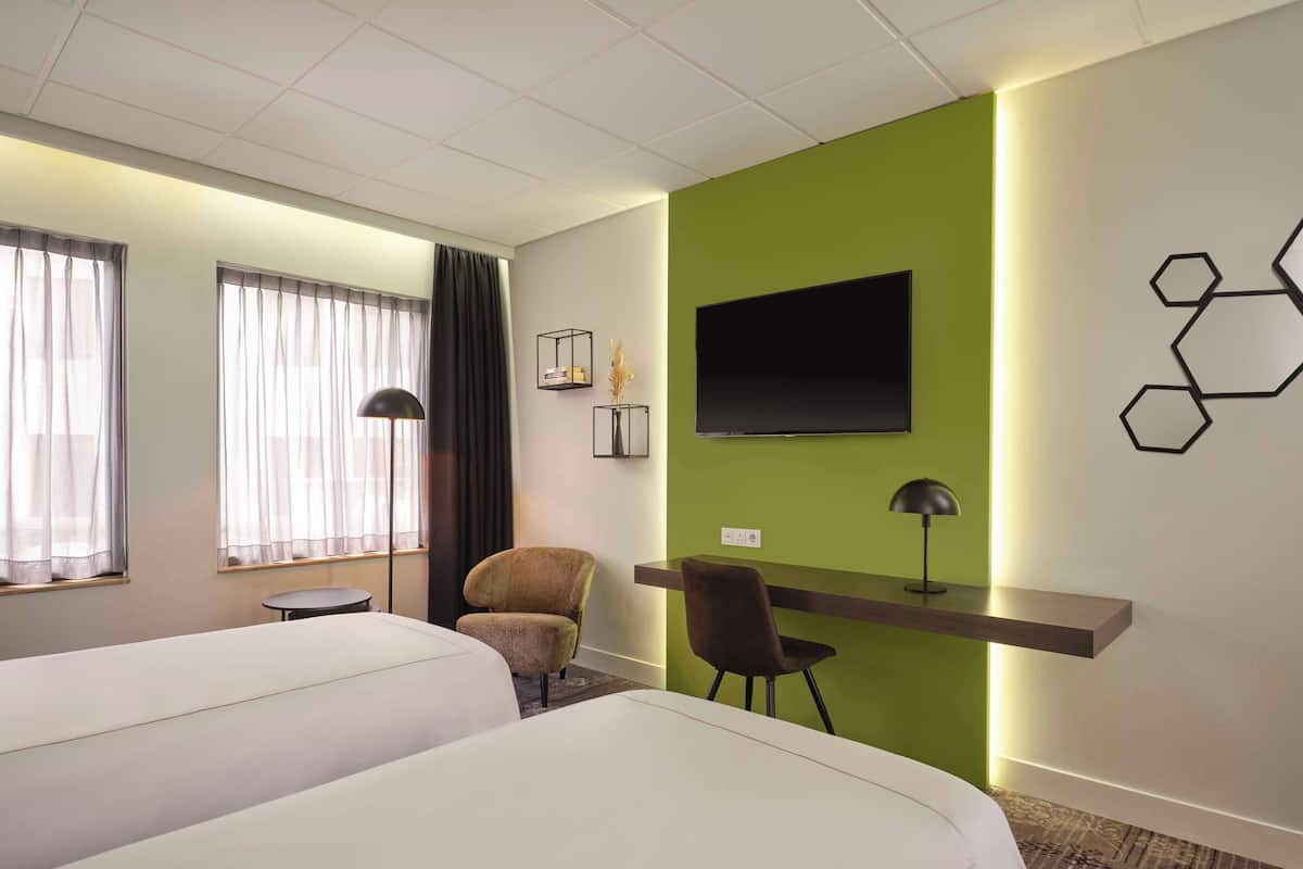 Une chambre d’hôtel avec deux lits, un bureau, une chaise, une télévision et un mur d’accent vert.