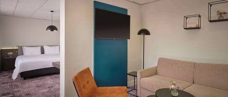 A hotel room with a bed, a sofa, a chair, a small table, and a TV.