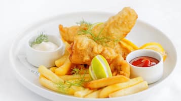 A plate of fish and chips with lemon wedges, tartar sauce, and ketchup.