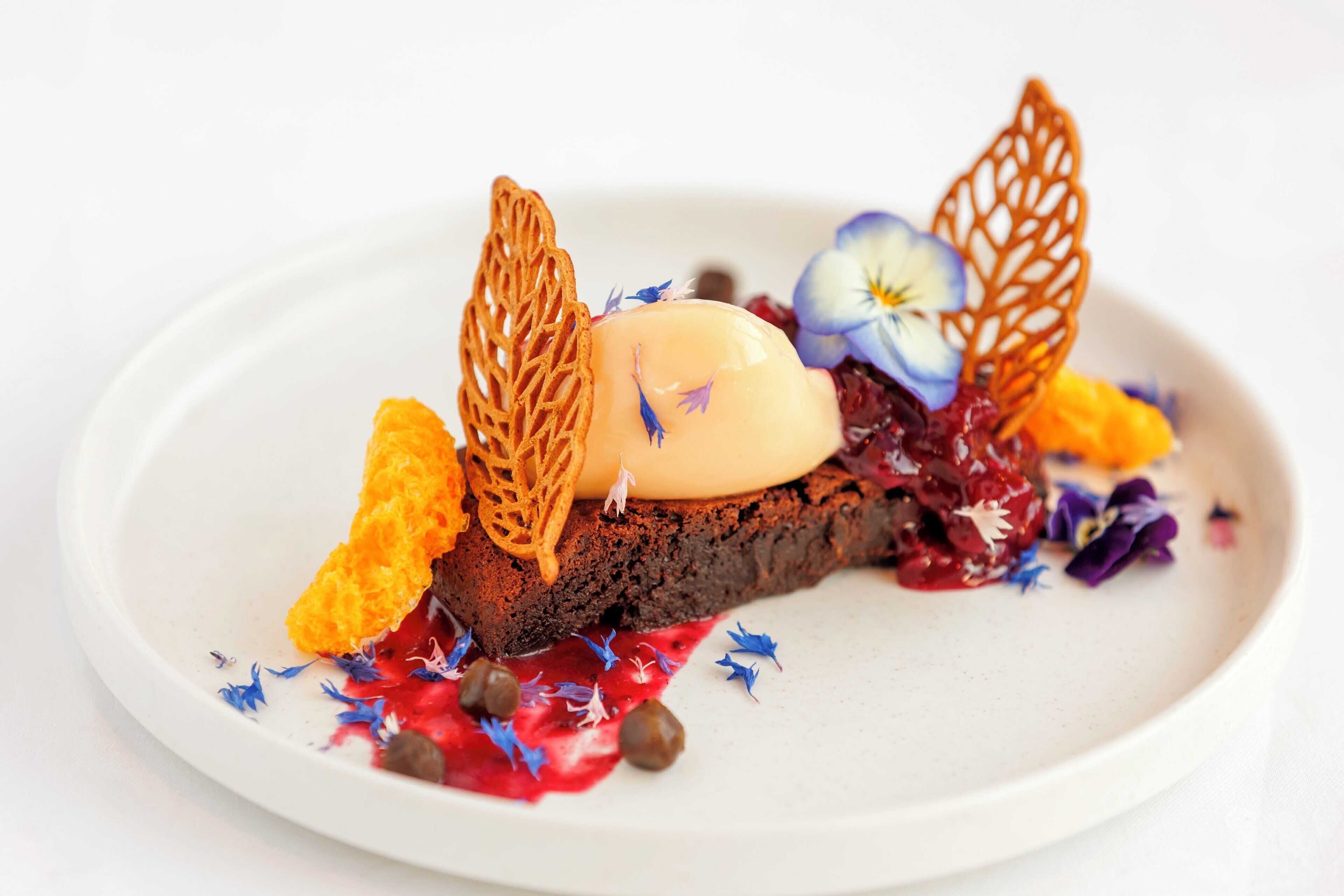 A dessert with a chocolate base, topped with a creamy element, orange zest, and decorative leaves.