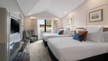 Habitación de hotel con dos camas, televisión, escritorio y vista al exterior.