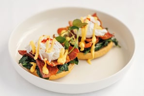 Two poached eggs on toast with spinach, bacon, and hollandaise sauce.